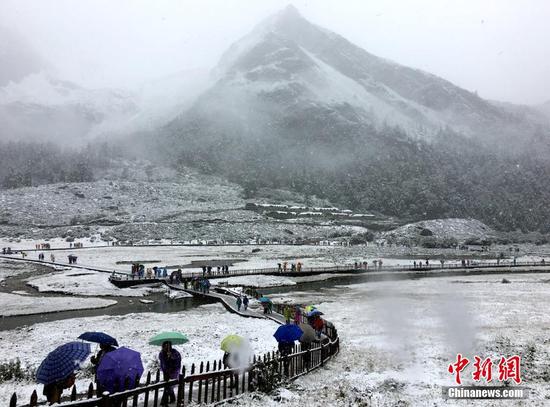 9月20日，受冷空氣影響，四川甘孜州稻城亞丁景區(qū)雪花飄舞，大霧彌漫，山峰披上白紗，銀裝素裹。正在景區(qū)內(nèi)游玩的海內(nèi)外游客紛紛用手機記錄雪景，并拍照留念。鐘欣 攝